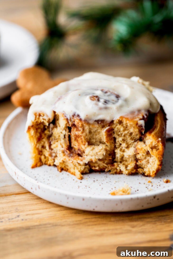 Spiced Gingerbread Swirl Buns 10 A single gingerbread cinnamon roll on a plate with a bite taken, showcasing its soft interior and generous icing.