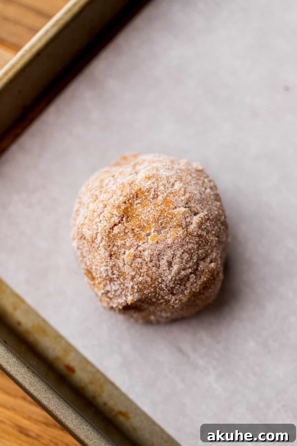 A perfectly portioned cookie dough ball, rolled in sugar, resting on a parchment-lined cookie sheet before baking.