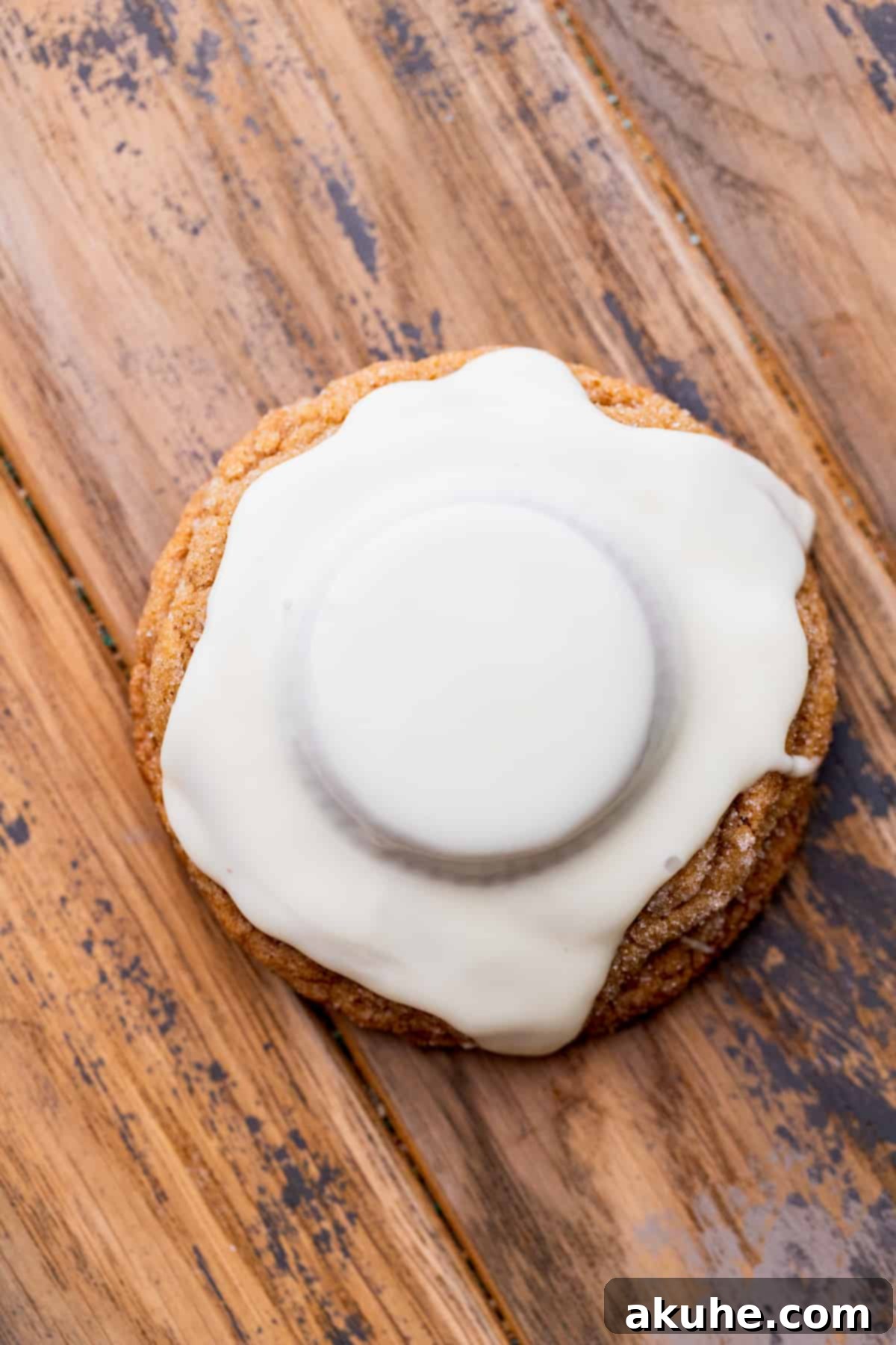 Melted white chocolate poured over a peanut butter cup on a gingerbread cookie, creating the melted snowman base.