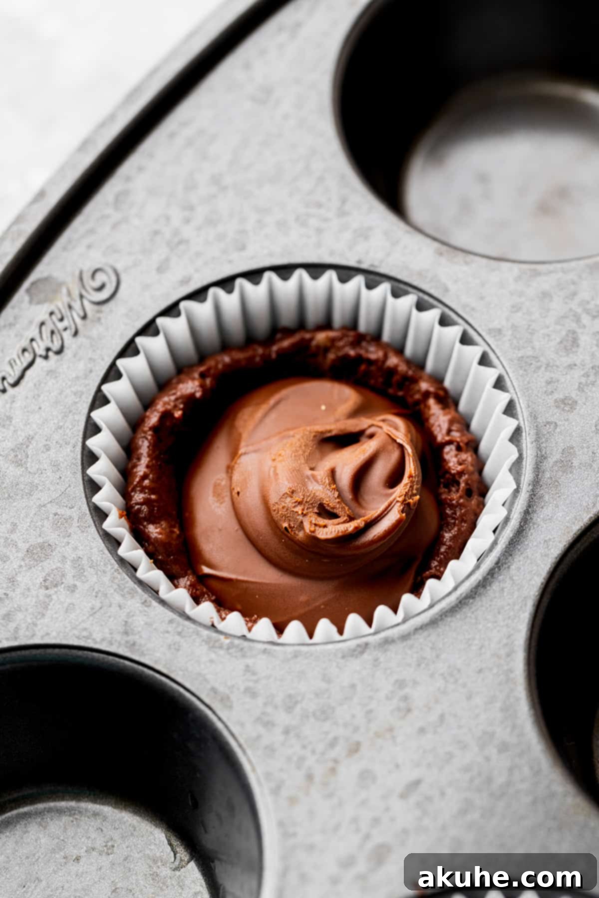 A frozen dollop of Nutella carefully placed on top of the first layer of muffin batter in a paper liner.