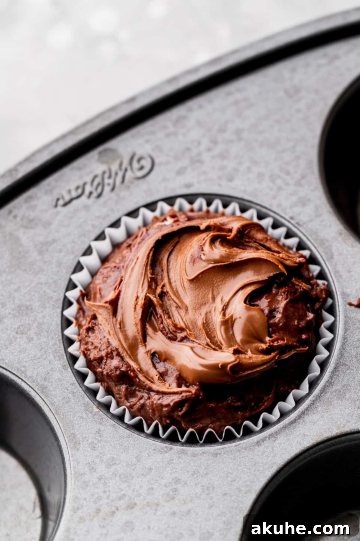 Close-up of muffin batter in a pan, topped with a delicate Nutella swirl created with a butter knife.