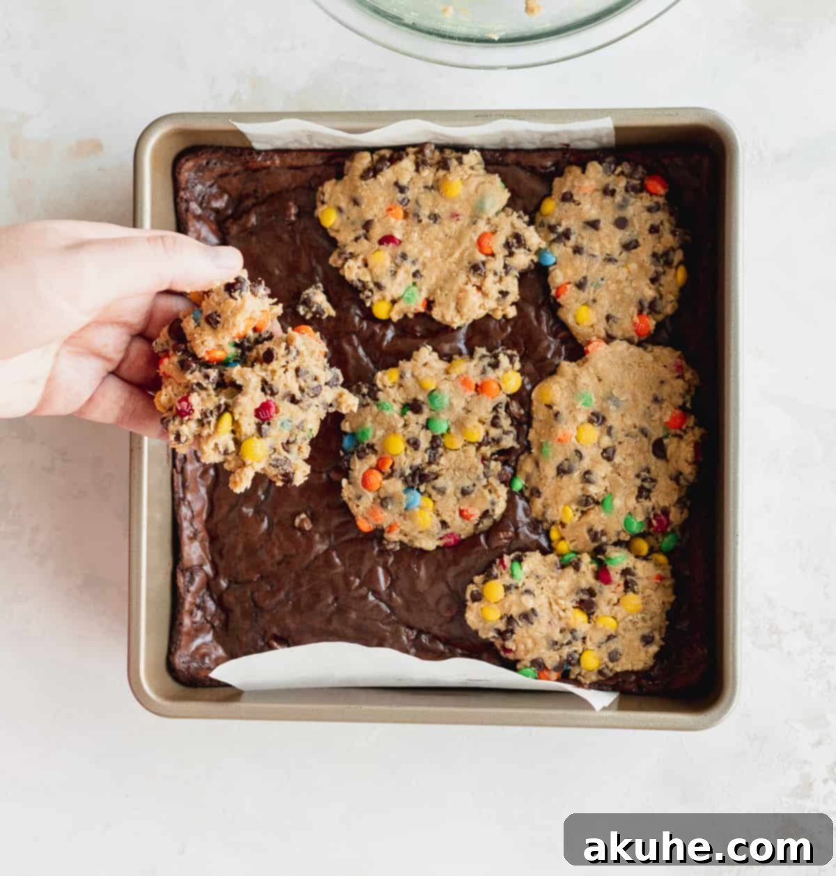Fudgy Monster Cookie Brownies 5 Expertly placing flattened discs of monster cookie dough onto the partially baked fudgy brownie layer in a baking pan.