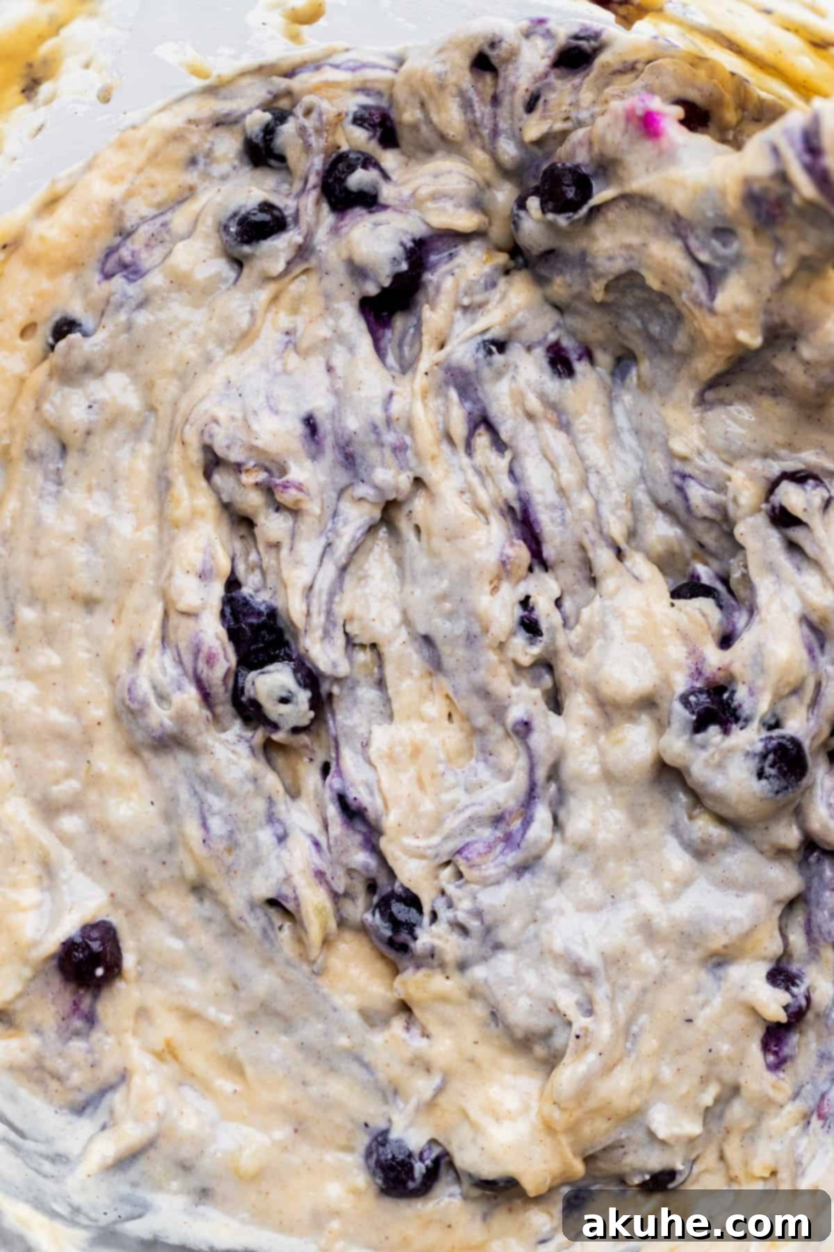 Irresistible Banana Blueberry Muffins 6 Fully mixed banana blueberry muffin batter in a large glass bowl, showing the distribution of blueberries.