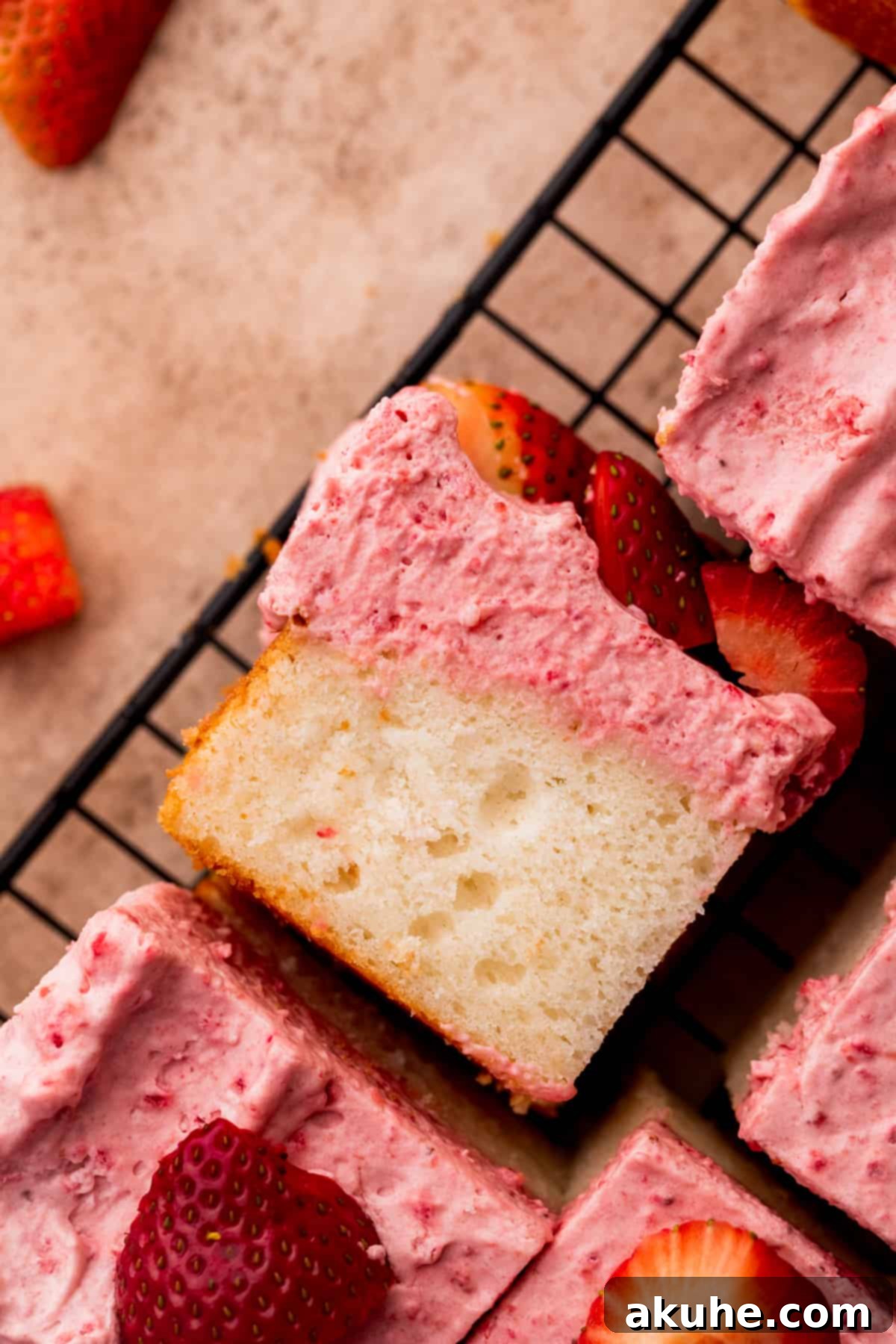 A perfectly sliced piece of strawberry mousse cake, showcasing its light white cake base and fluffy pink mousse, topped with a fresh strawberry, resting on a wire rack.