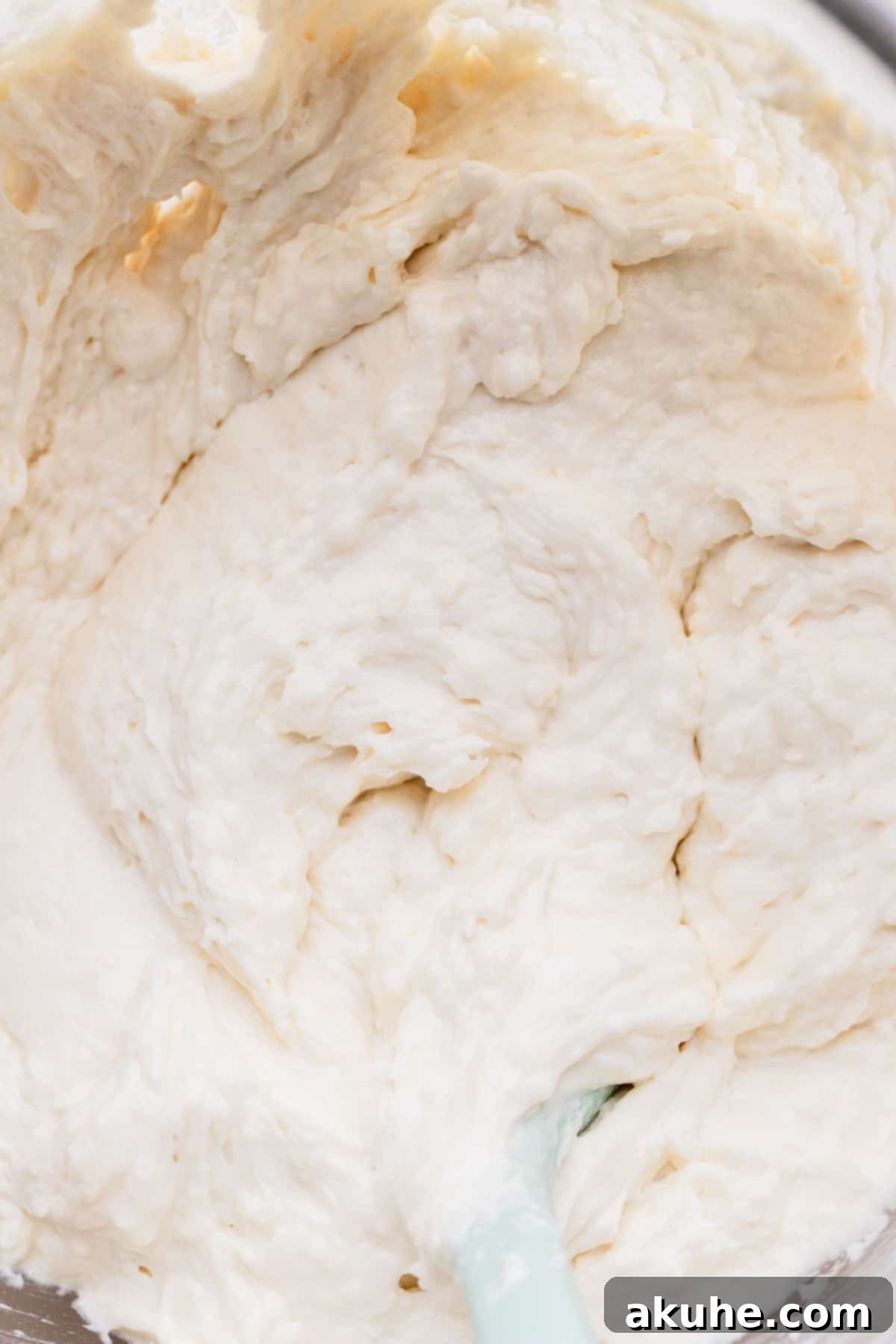A close-up of light, fluffy white cake batter in a clear glass bowl, showcasing its smooth texture before baking.