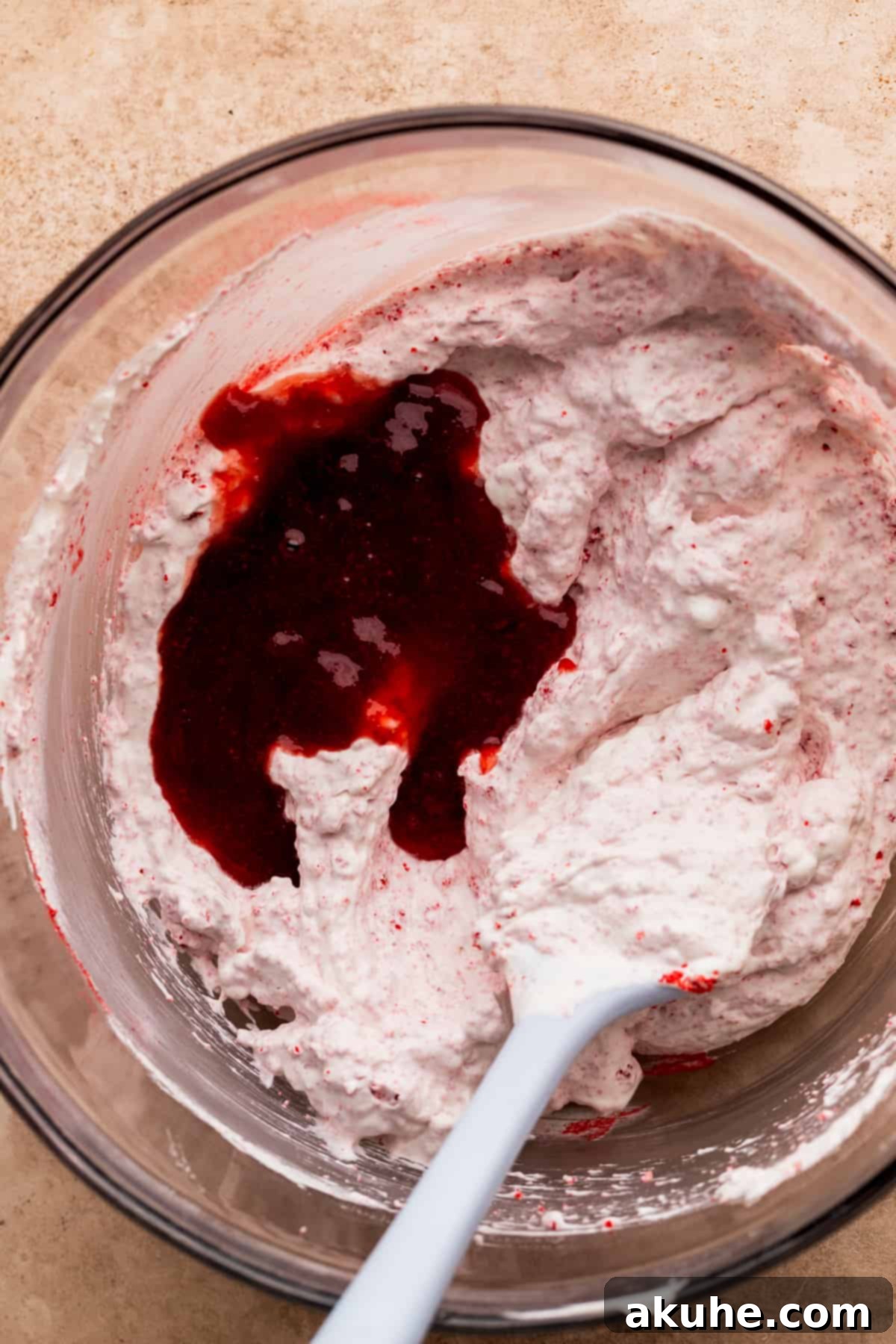 A bowl of freshly whipped heavy cream with a vibrant strawberry sauce gently swirled on top, ready to be folded into a mousse.
