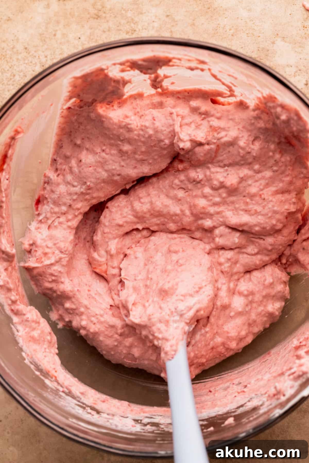 A bowl of creamy, light pink strawberry mousse, perfectly aerated and ready to be spread onto the cake base.