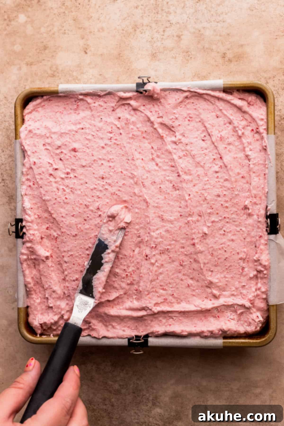 A luscious layer of pink strawberry mousse spread evenly over the white cake base in a baking pan, ready for chilling.