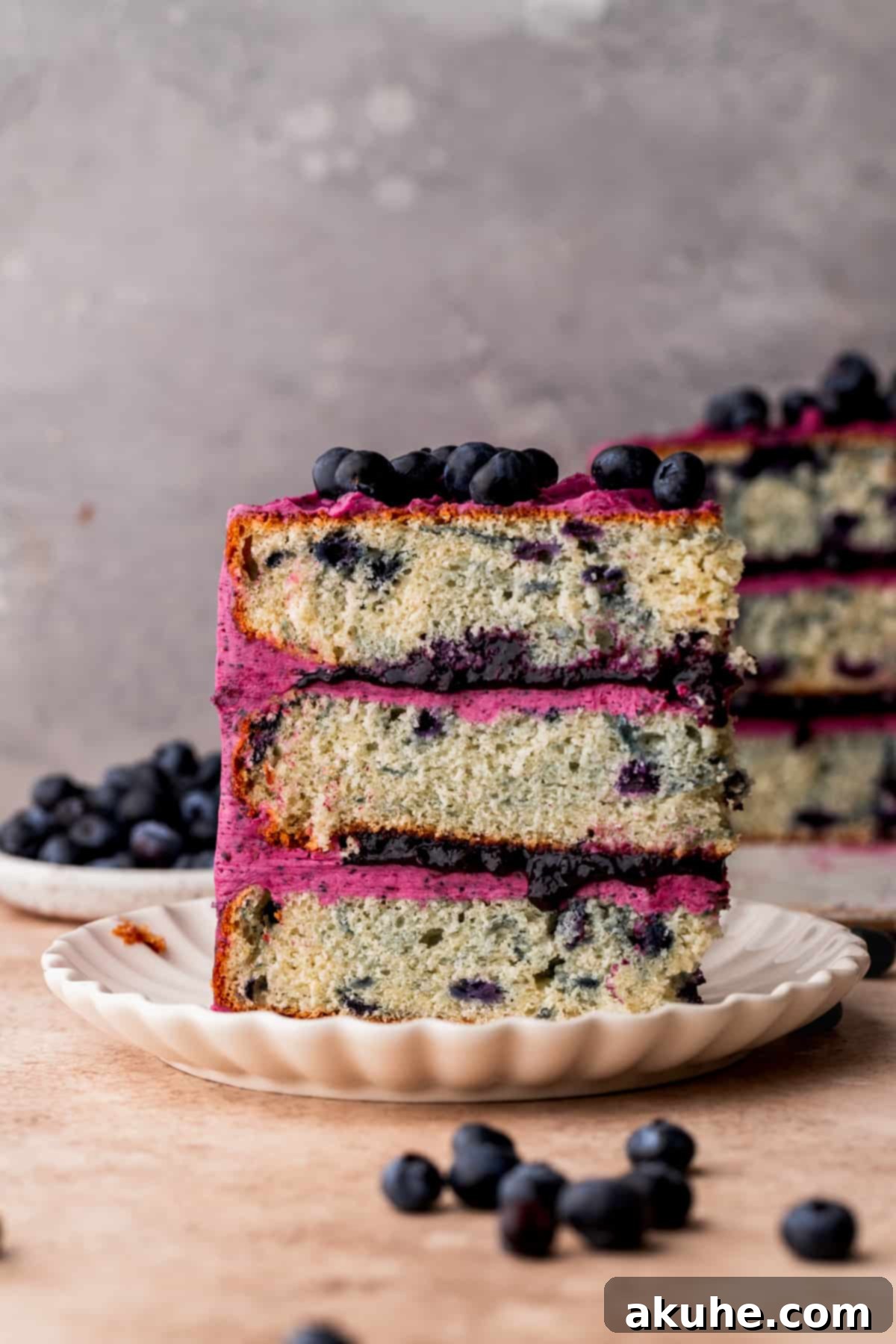 Bursting Berry Bliss 3 A perfectly portioned slice of moist blueberry cake standing on a white plate, showcasing its beautiful layers.