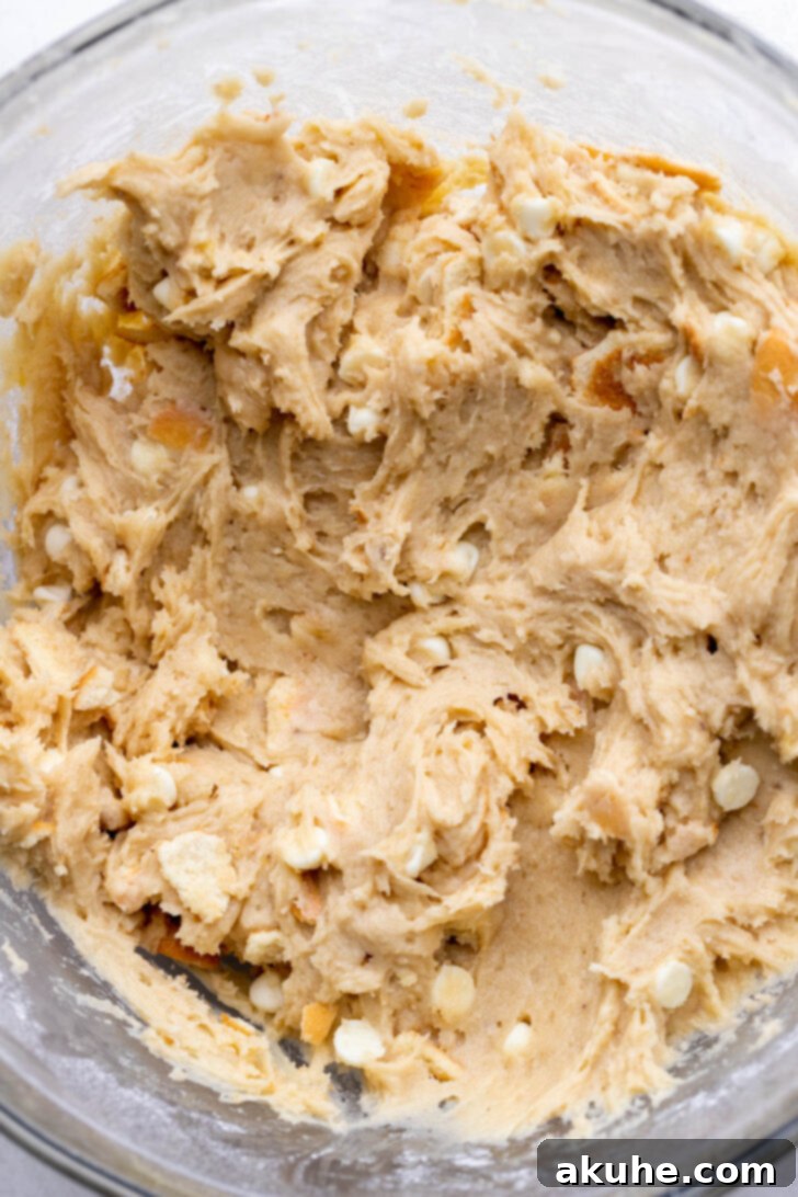 The Ultimate Banana Pudding Cookies 5 Freshly mixed cookie dough in a bowl, with white chocolate chips and Nilla Wafer pieces visible.