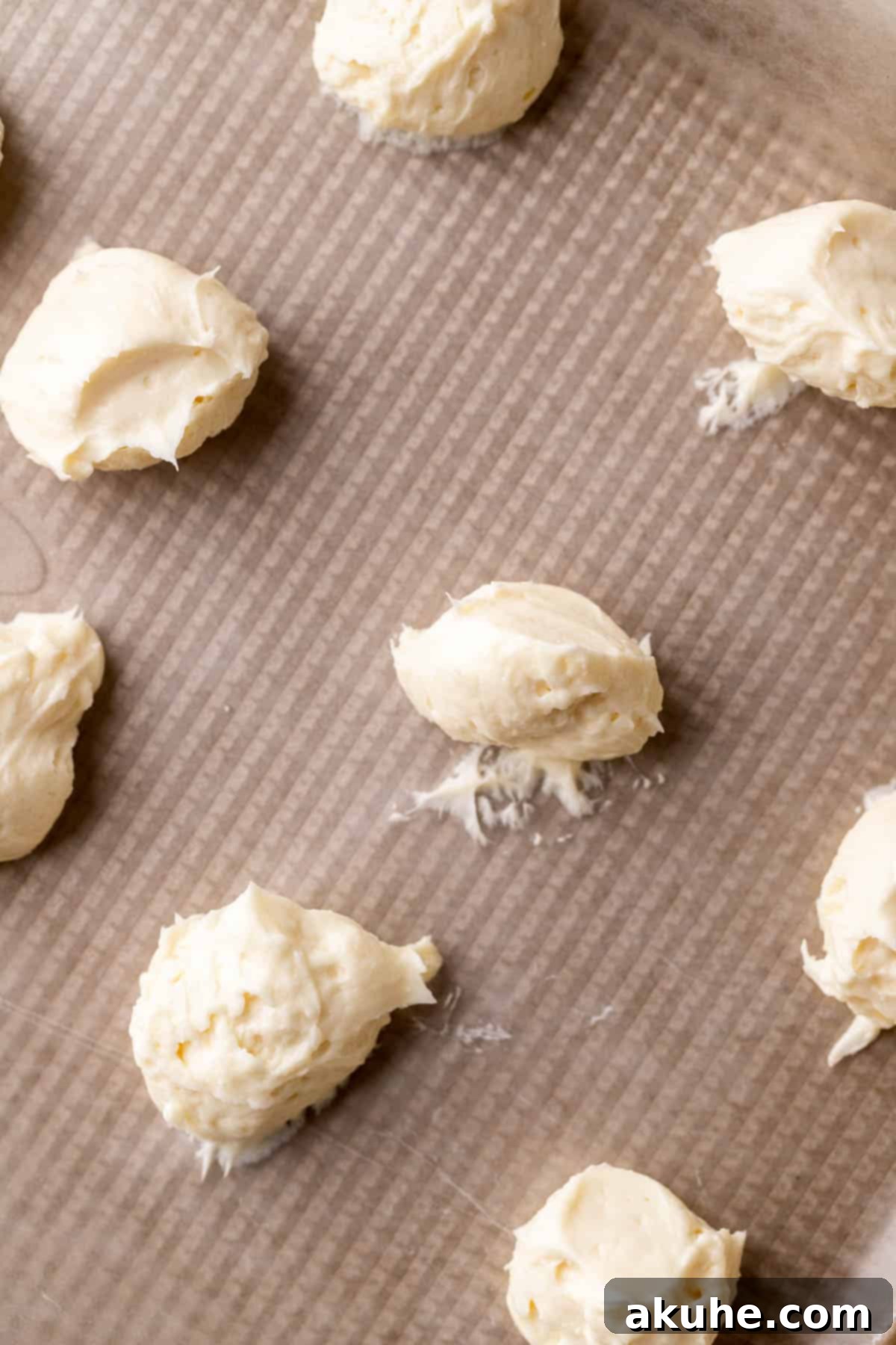 Cheesecake dollops neatly arranged on a wax paper-lined cookie sheet.