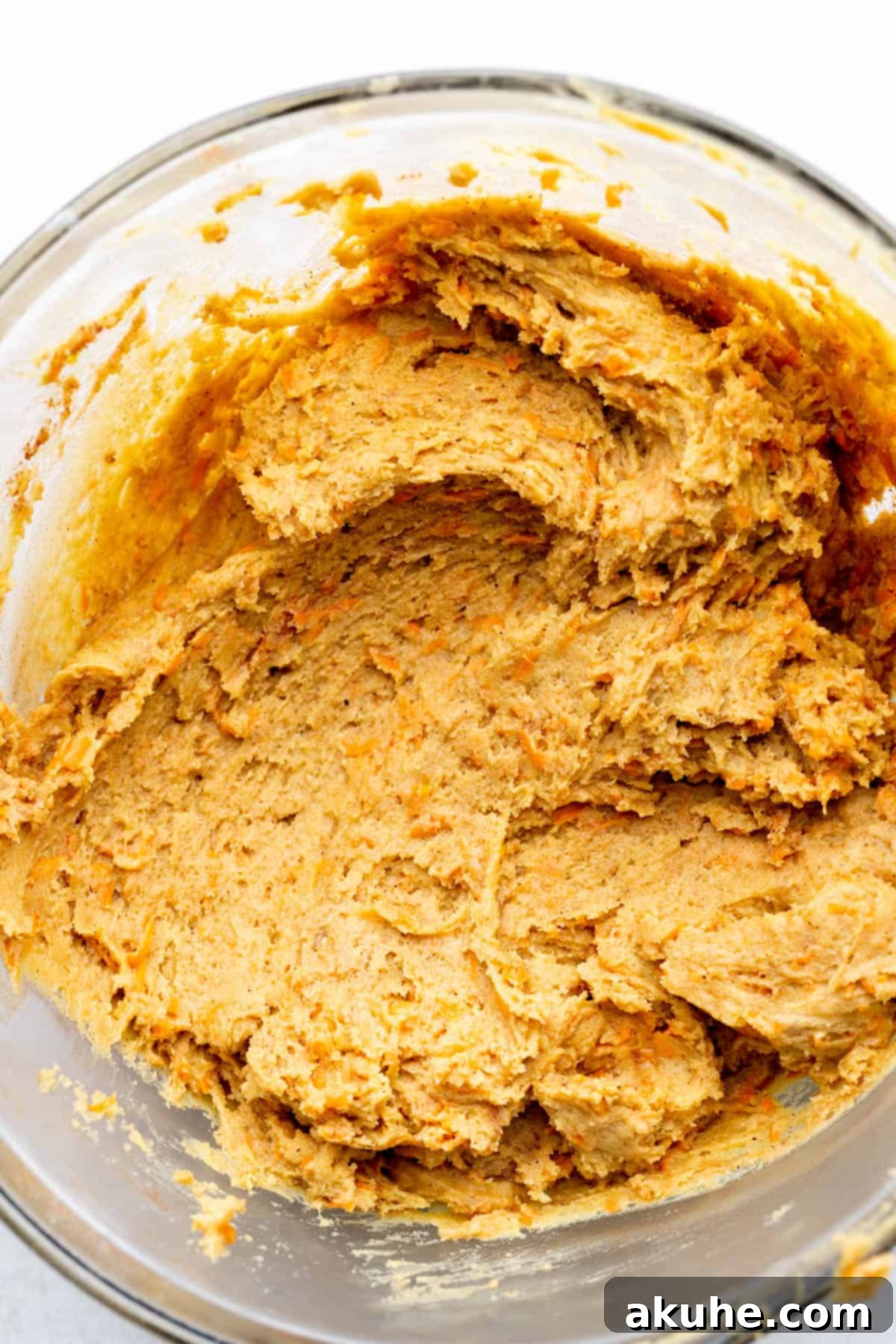 Carrot cake cookie dough with visible grated carrots in a glass bowl.