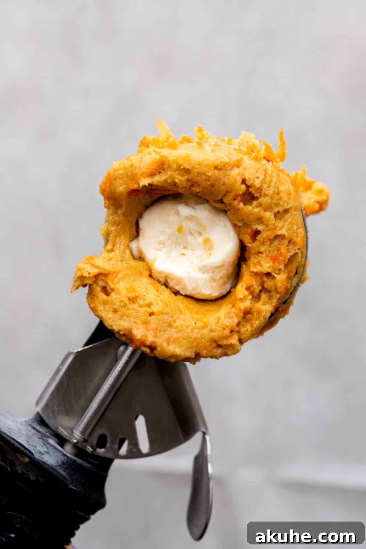 Carrot cake cookie dough in a scoop, carefully being filled with cheesecake.