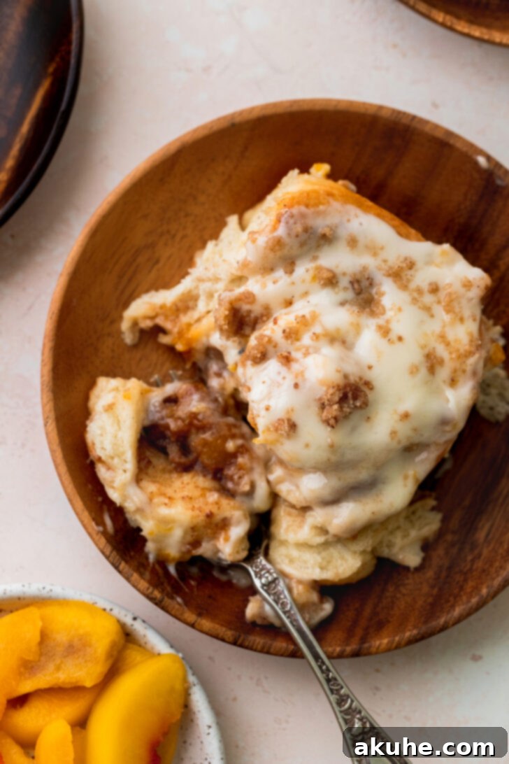 Peach Cobbler Cinnamon Rolls Reimagined 11 Top view of a single peach cobbler cinnamon roll on a white plate, showcasing its melted icing and crumbly topping, ready to be eaten.