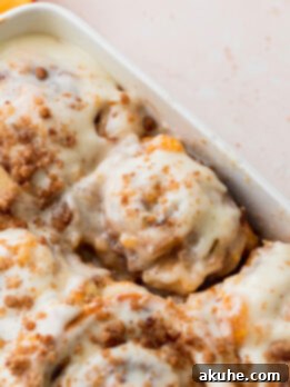 Peach Cobbler Cinnamon Rolls Reimagined 12 Close-up of baked peach cobbler cinnamon rolls in a pan, glistening with icing.