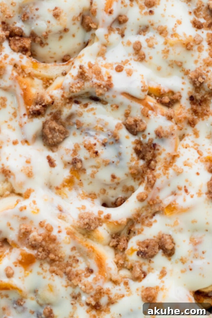 Peach Cobbler Cinnamon Rolls Reimagined 3 Top view of fluffy peach cobbler cinnamon rolls in the pan, showing the golden crumb topping and creamy icing.