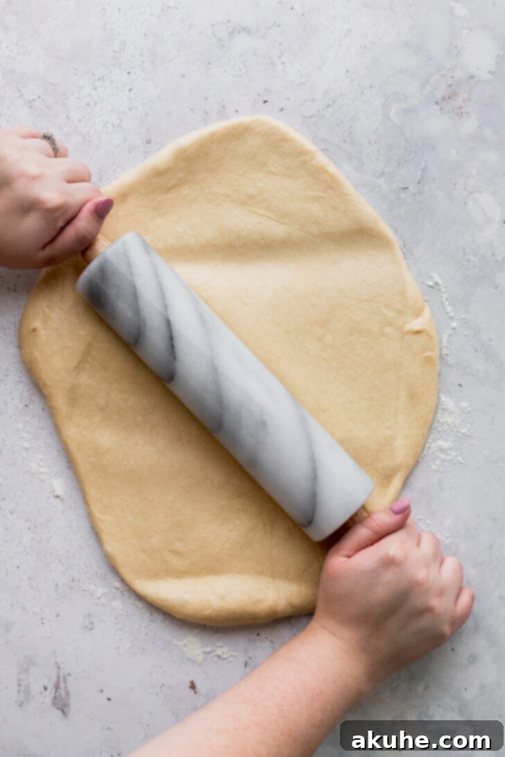 Peach Cobbler Cinnamon Rolls Reimagined 4 Dough being rolled out evenly into a rectangular shape on a lightly floured surface, preparing for the fillings.