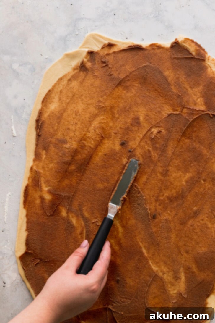 Peach Cobbler Cinnamon Rolls Reimagined 5 Smooth cinnamon filling being spread generously across the rolled-out dough, creating the first flavorful layer.