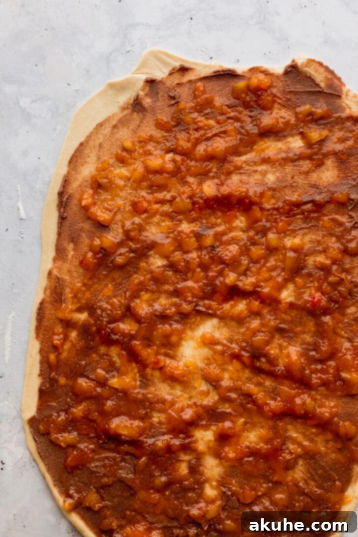 Peach Cobbler Cinnamon Rolls Reimagined 6 Lush peach jam being spread over the cinnamon filling on the dough, adding the signature cobbler element.