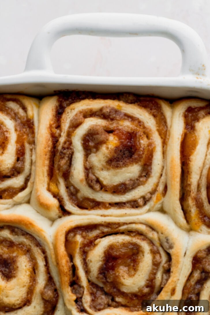 Peach Cobbler Cinnamon Rolls Reimagined 9 Golden brown peach cobbler cinnamon rolls, freshly baked and steaming in the pan, indicating they are cooked through.