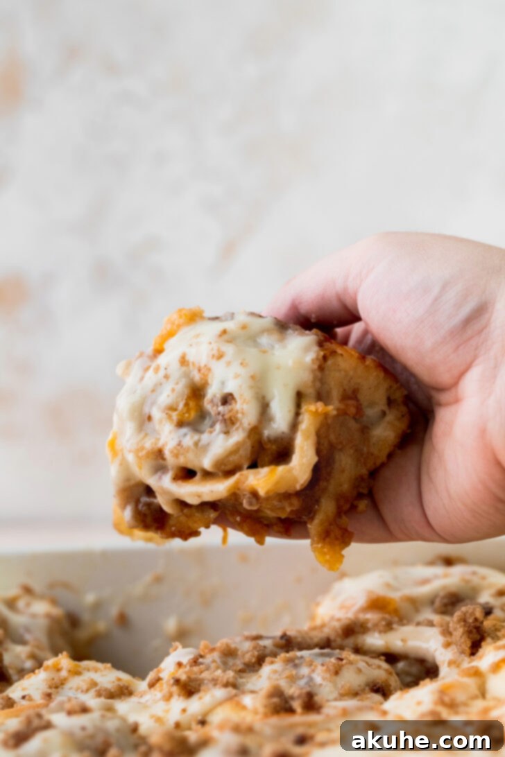 Peach Cobbler Cinnamon Rolls Reimagined 10 A hand reaching for a warm peach cobbler cinnamon roll, pulling it from the pan, highlighting its soft texture.