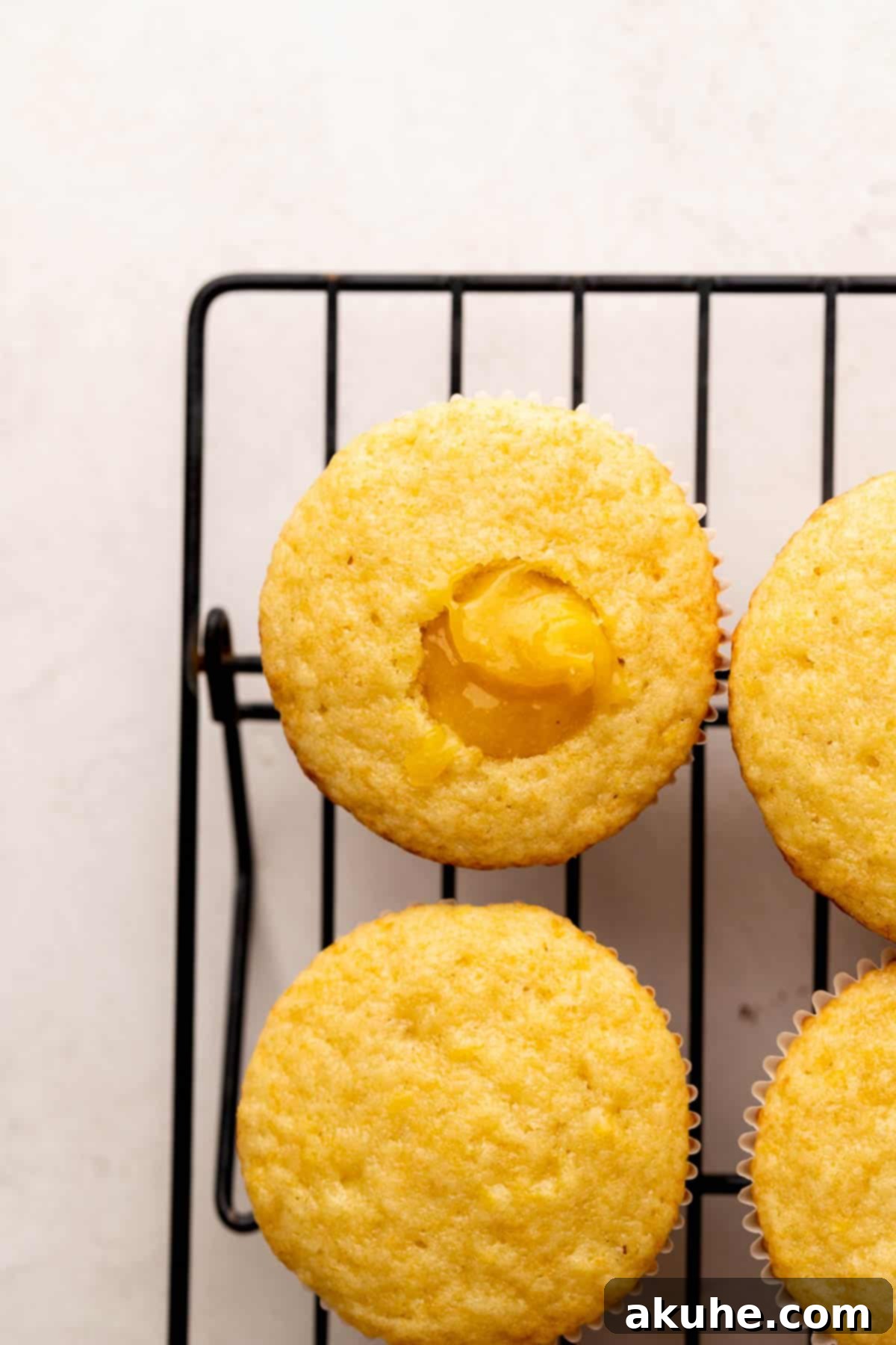A lemon bar cupcake with a spoonful of bright yellow lemon filling placed into its cored center.