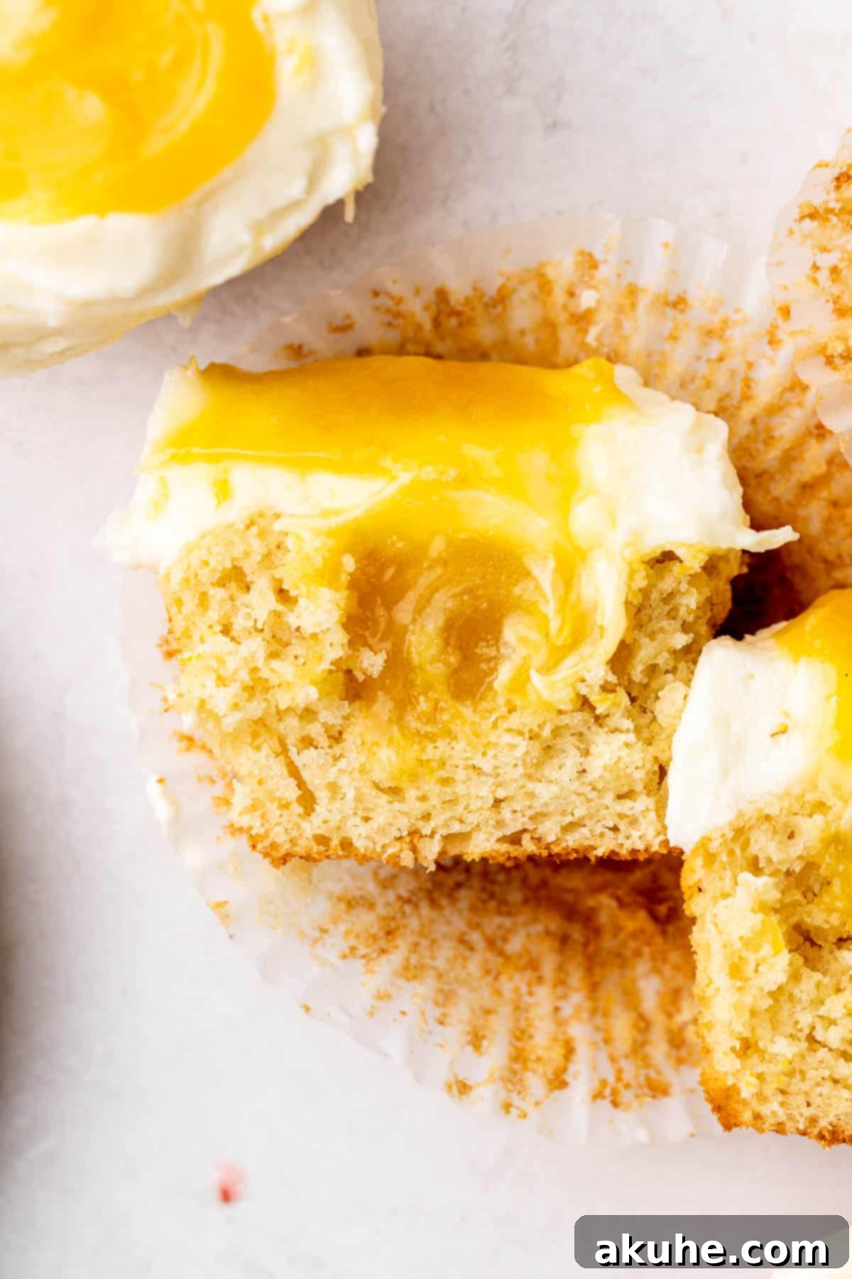 A lemon bar cupcake sliced in half, clearly showing the moist cake, lemon filling, and creamy frosting layers.