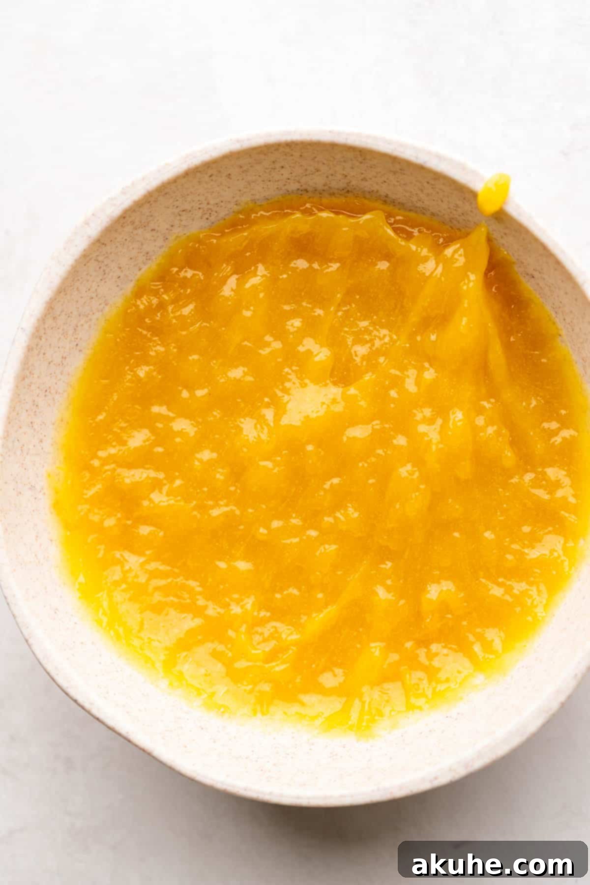 Smooth and thick lemon bar filling cooling in a bowl, covered with plastic wrap.