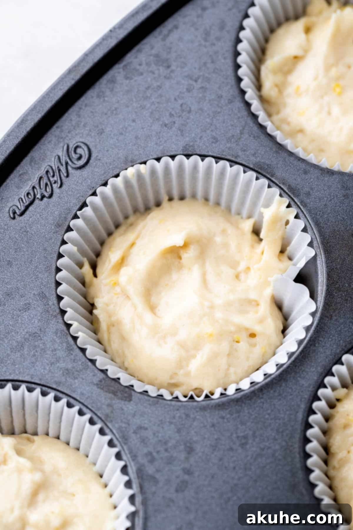 Unbaked lemon cupcake batter perfectly portioned into a cupcake tin with paper liners.