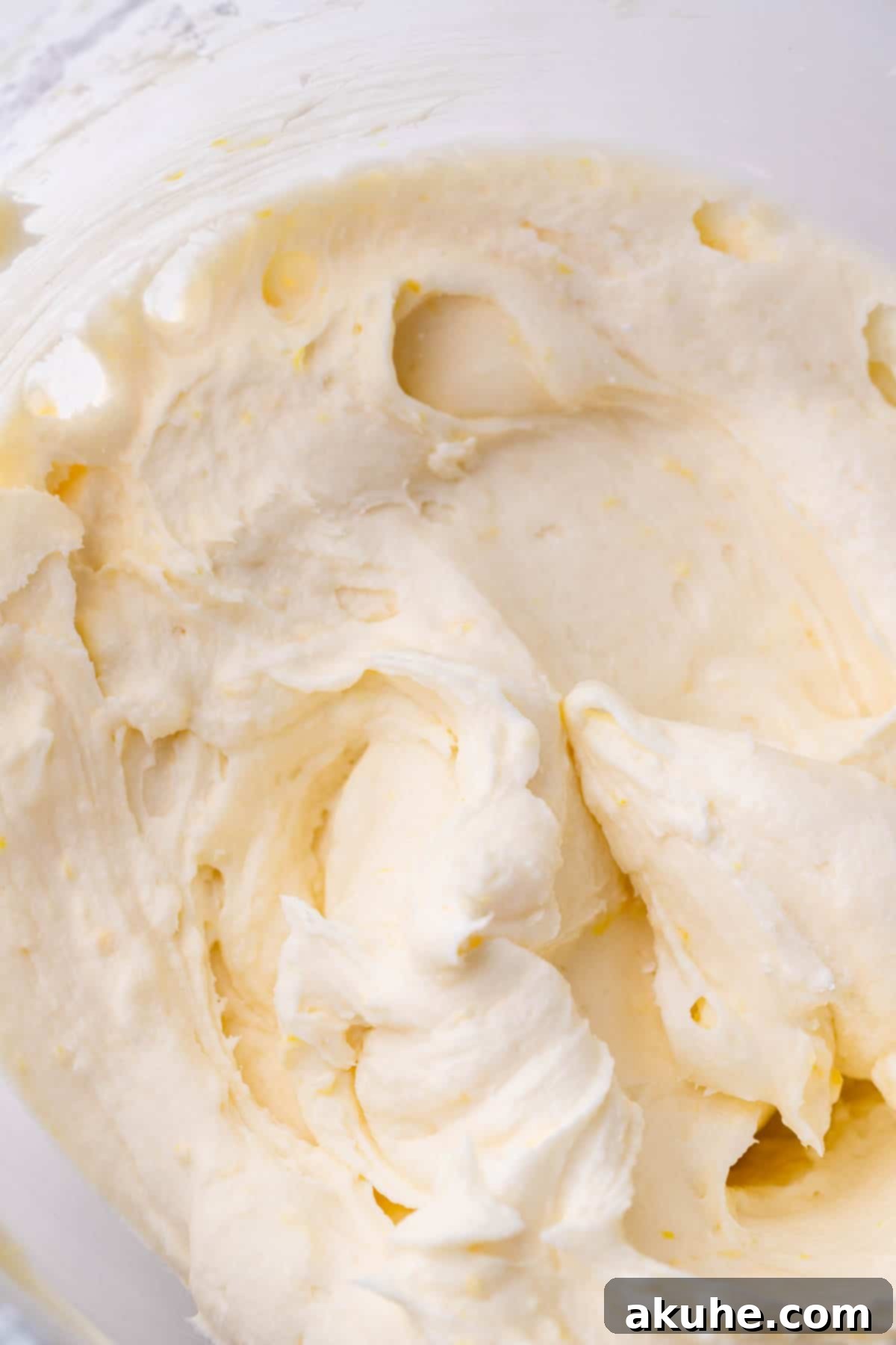 Smooth and creamy lemon cream cheese frosting in a clear glass mixing bowl.