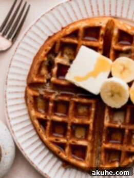 Banana waffles on a plate topped with butter, syrup, and bananas.