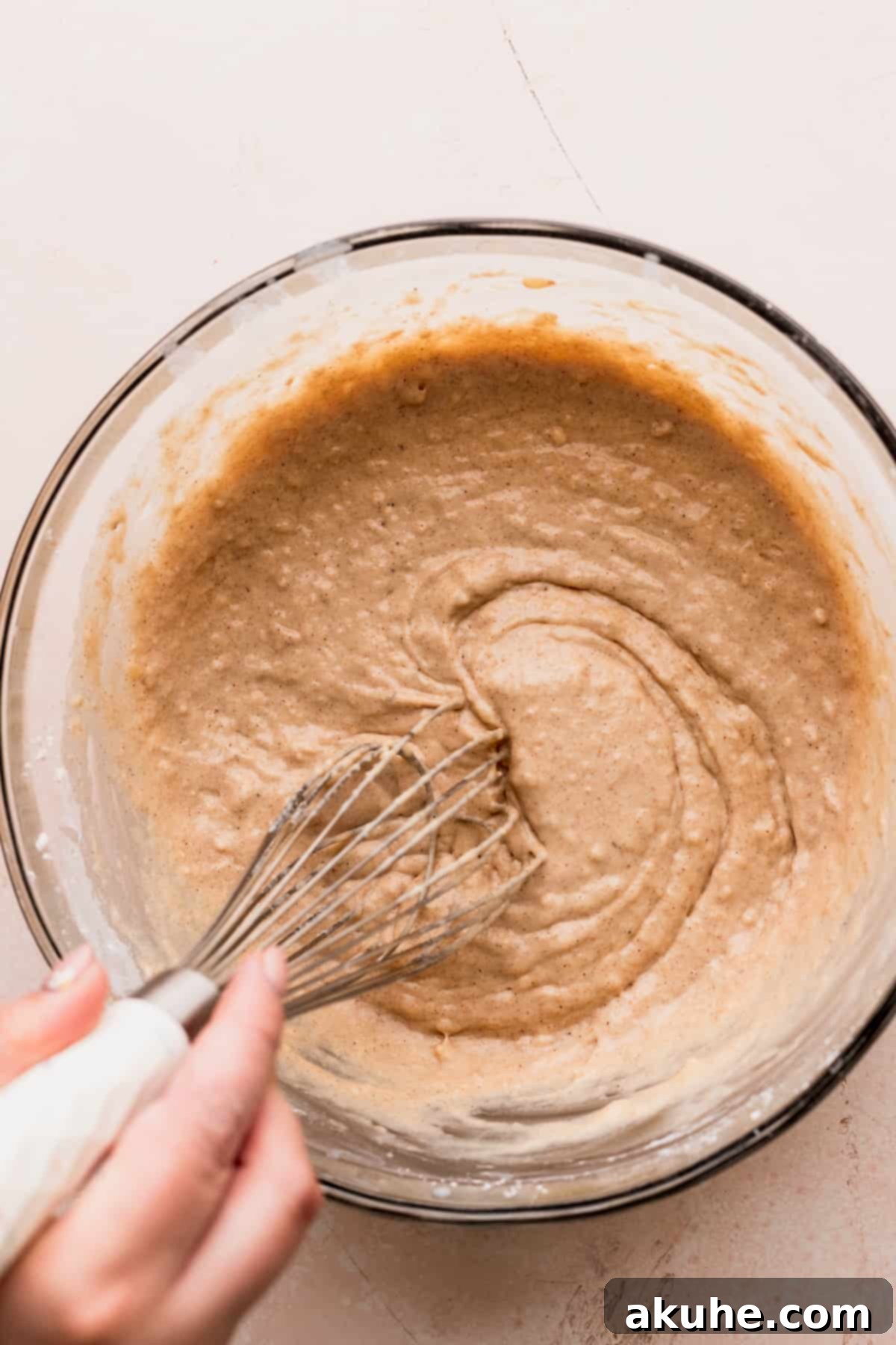 Waffle batter being gently mixed in a glass bowl, showing its thick yet slightly lumpy consistency.