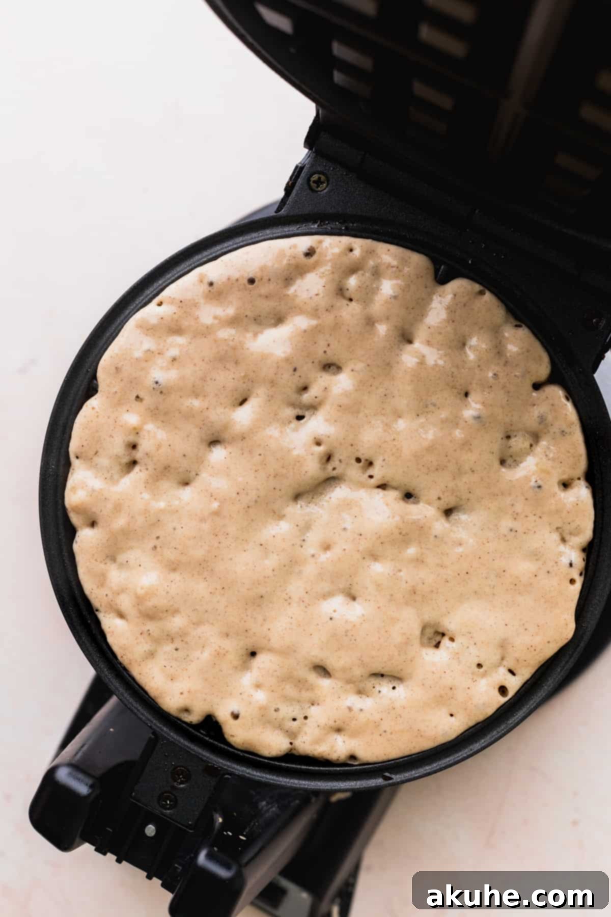 A ladle pouring rich banana waffle batter into a preheated waffle iron, ready for cooking.