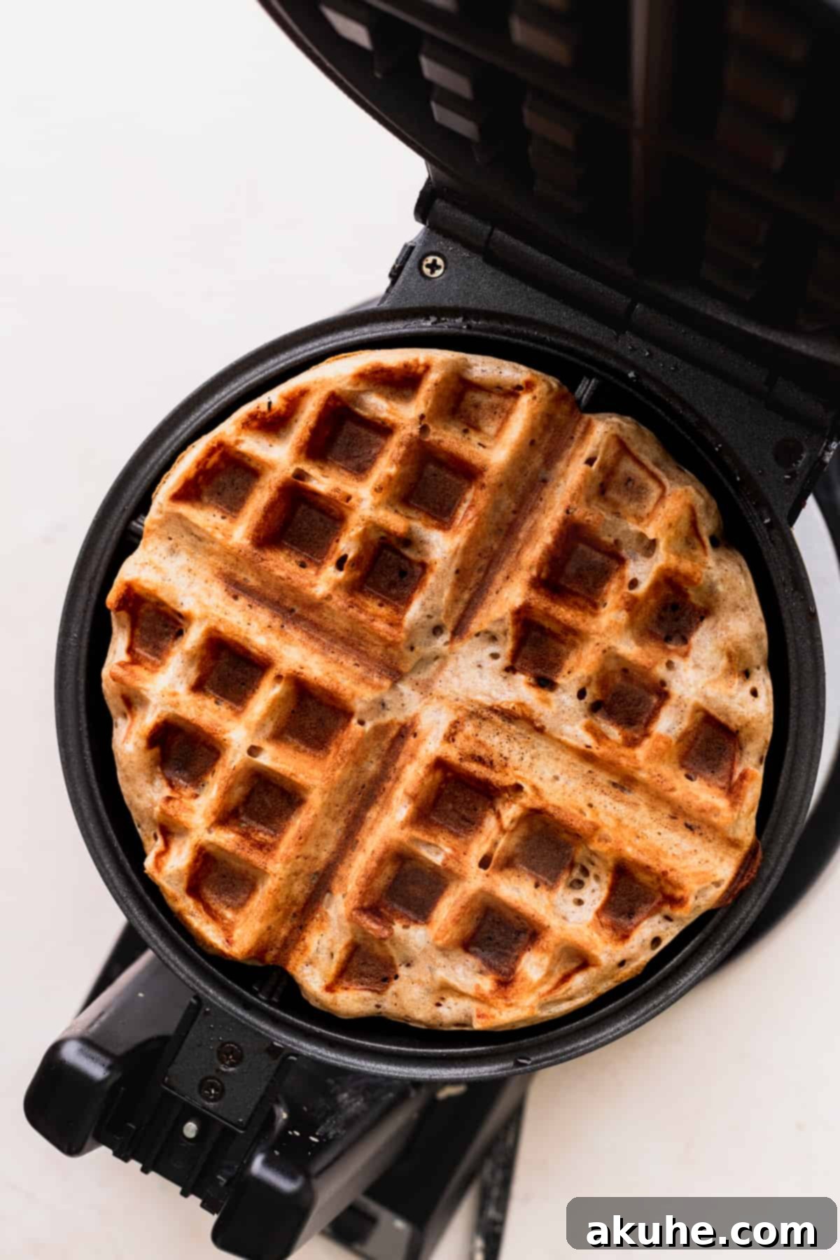 A freshly baked, golden-brown waffle in the waffle maker, steam gently rising, signaling perfect doneness.