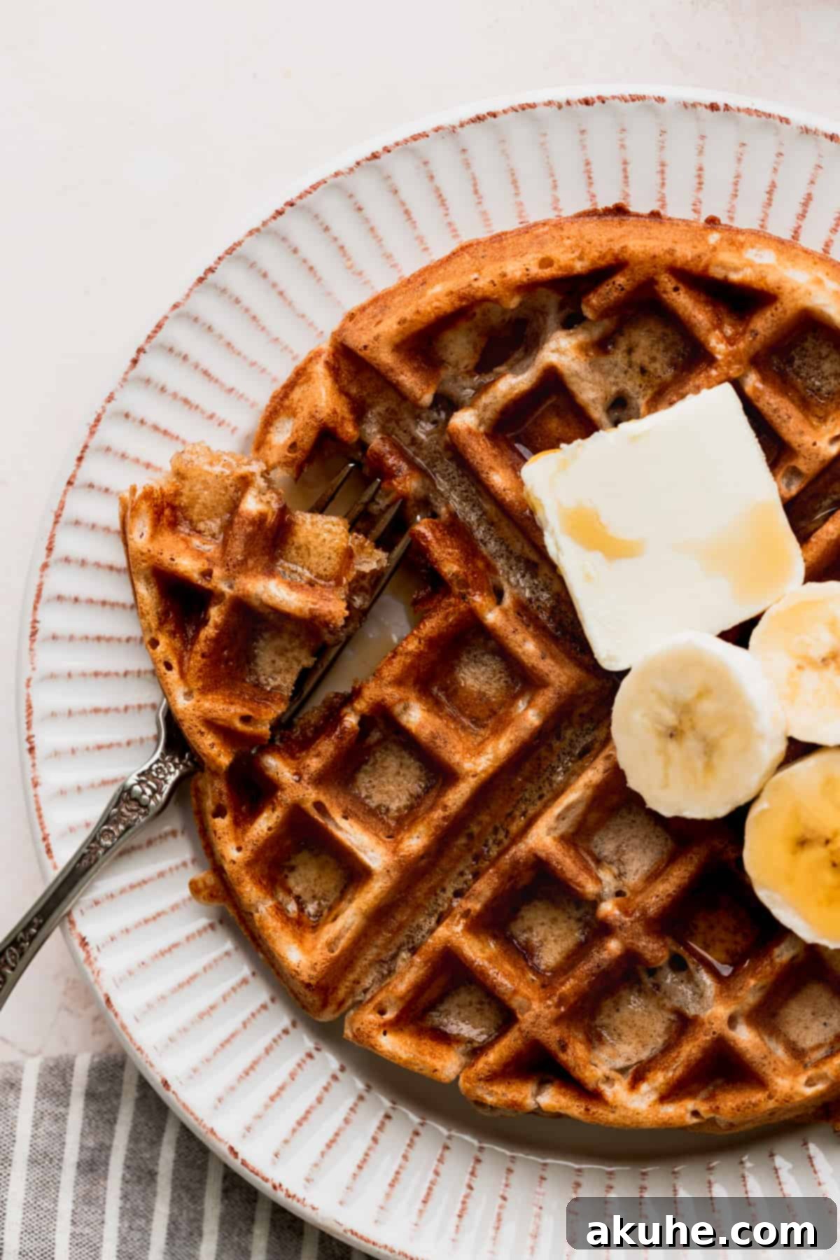 A person taking a bite out of a fluffy banana waffle, showing the soft interior.