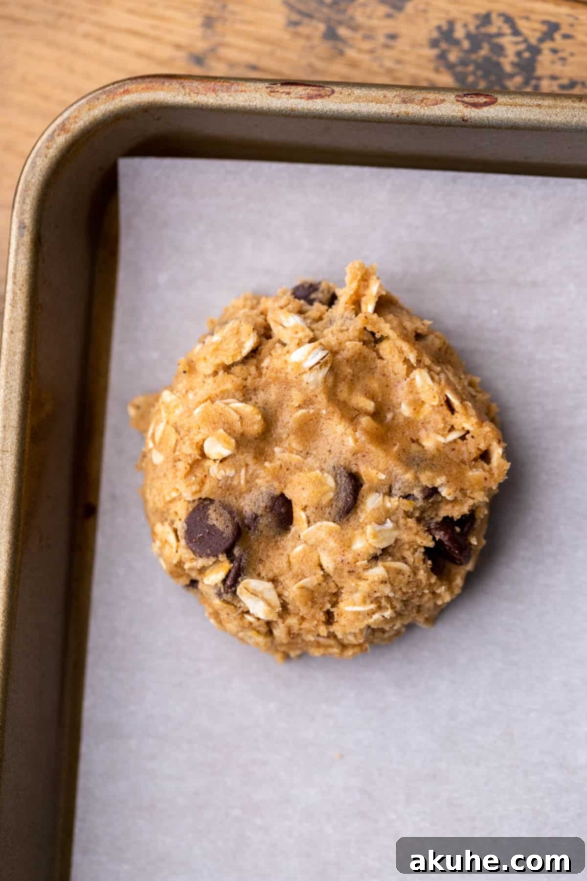 Hand gently pressing down a cookie dough ball on a baking sheet to flatten it slightly.