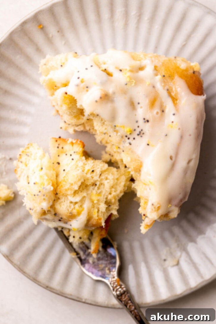 Sunshine Lemon Rolls 10 Close-up of a single lemon poppy seed roll on a plate, with a bite taken out, showing the soft interior and filling.