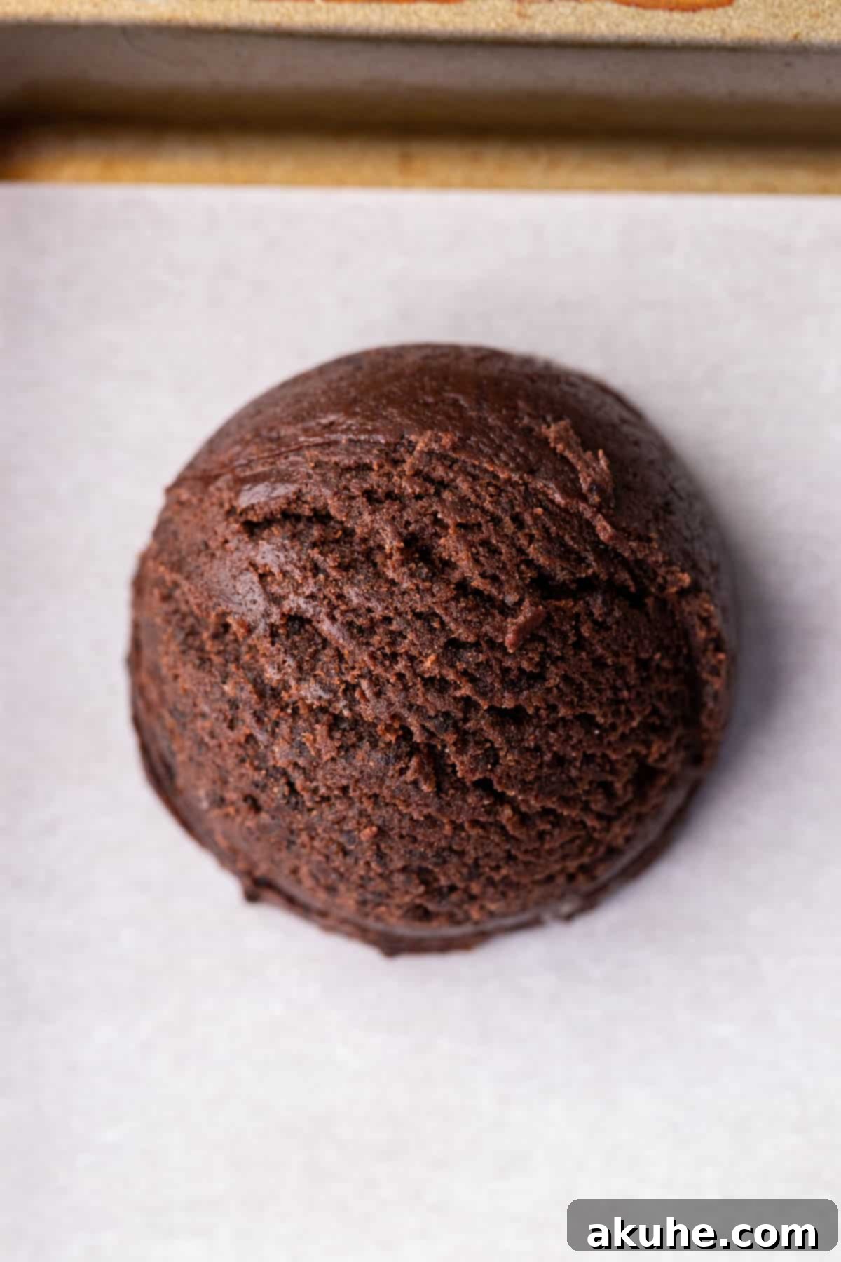 Raw chocolate cookie dough ball on a parchment-lined cookie sheet.