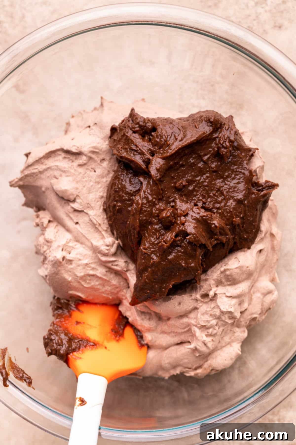 Chocolate pudding being folded into chocolate whipped cream in a glass bowl.