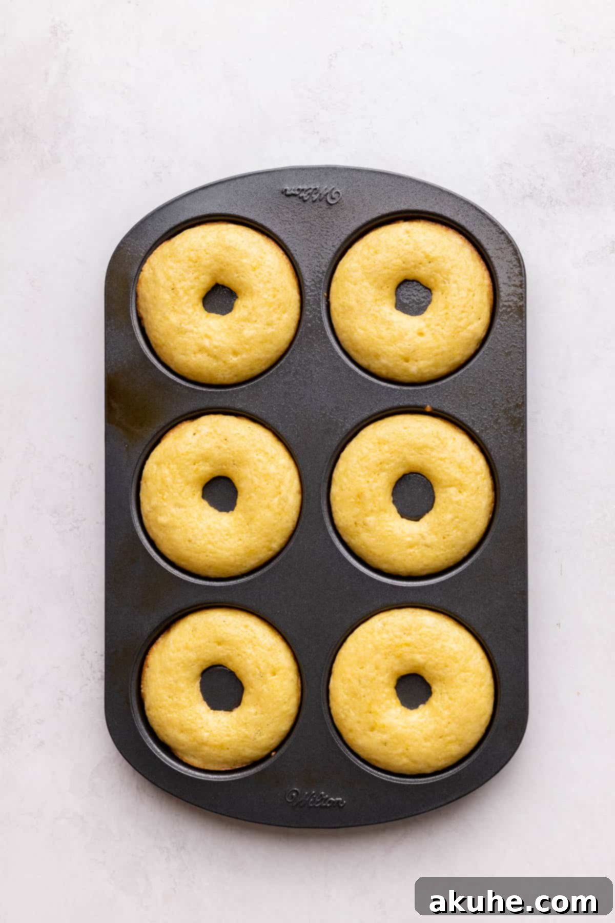 Zesty Lemon Donuts 7 Freshly baked donuts in a donut pan, golden and fluffy.