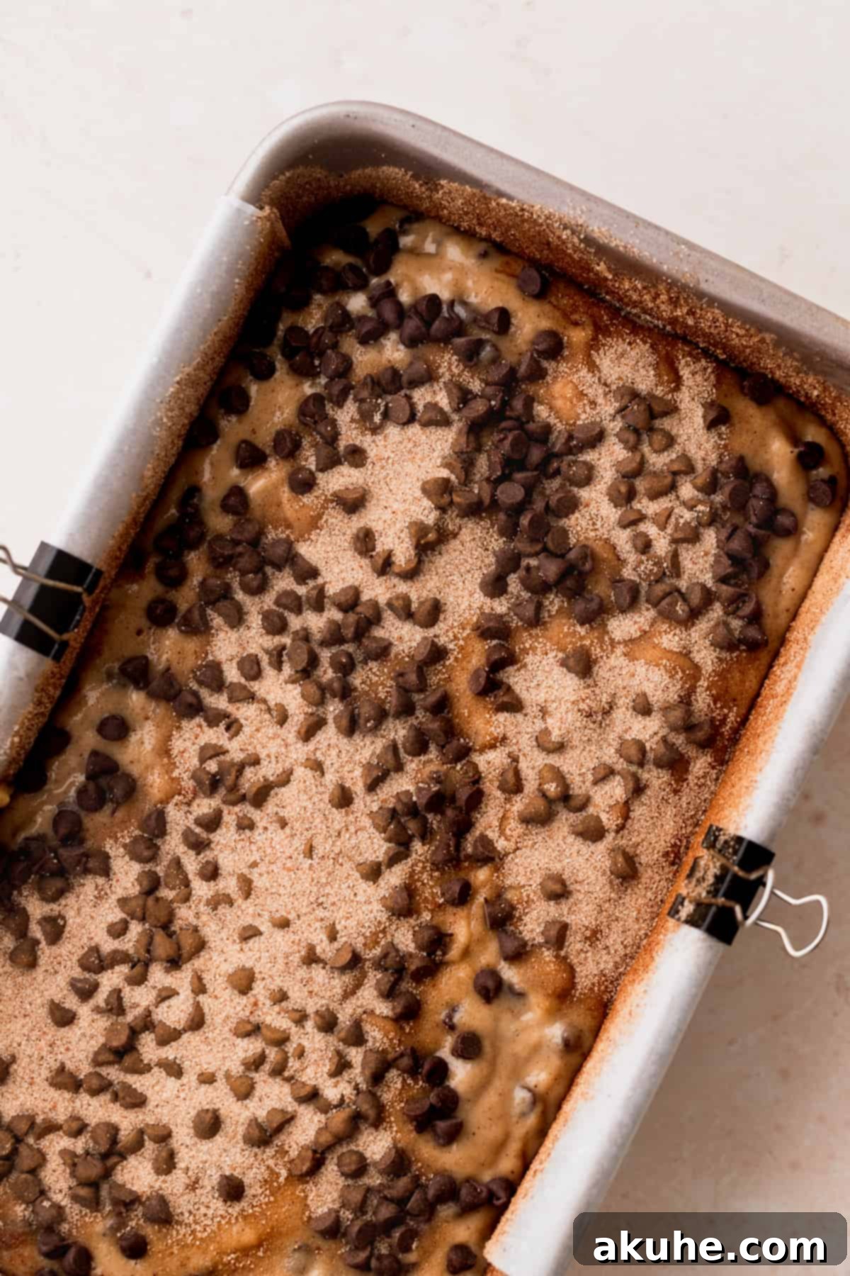 Cinnamon Swirl Chocolate Chip Banana Bread 7 Banana bread batter in a loaf pan, topped with cinnamon sugar and chocolate chips, ready for baking.