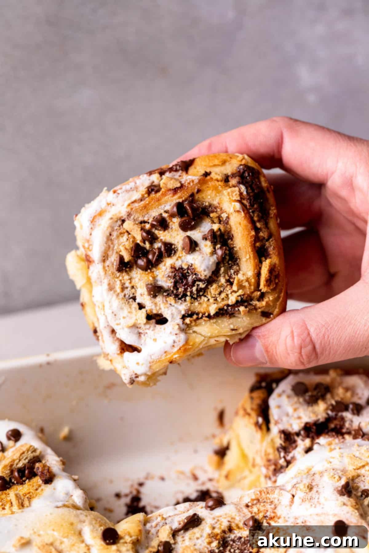 Gooey S'mores Cinnamon Buns 3 Taking one cinnamon roll out of the pan, showcasing its gooey center with melted chocolate and marshmallow.