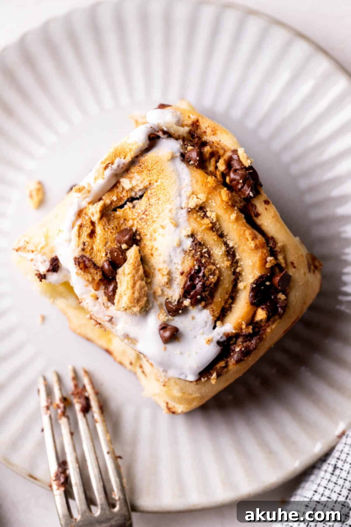 Gooey S'mores Cinnamon Buns 9 A single S'mores Cinnamon Roll on a plate, with a bite taken out, showing the gooey layers of chocolate, graham cracker, and cinnamon.