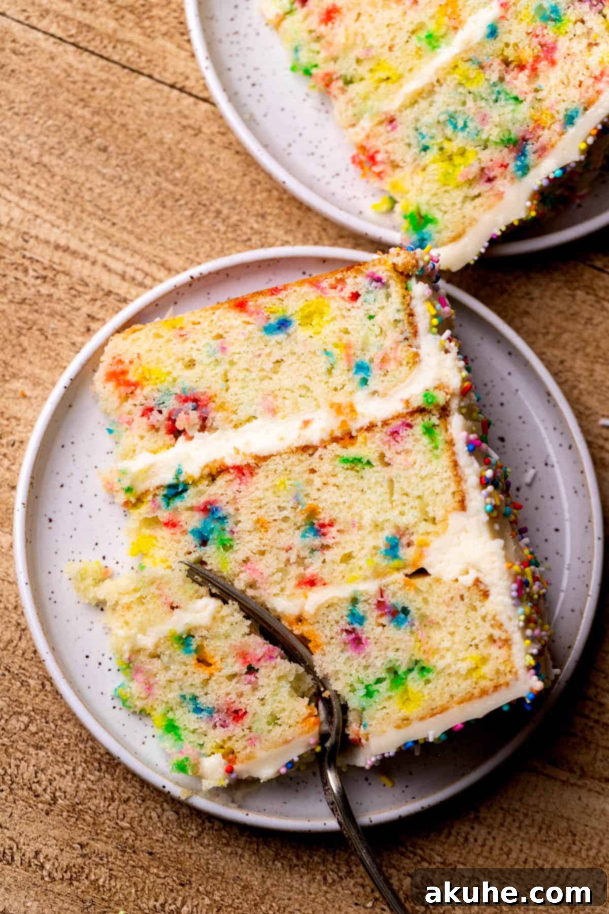 Festive Sprinkled Cake 2 Fork inserted into a slice of funfetti cake with cream cheese frosting on a white plate, showcasing the colorful sprinkles within.