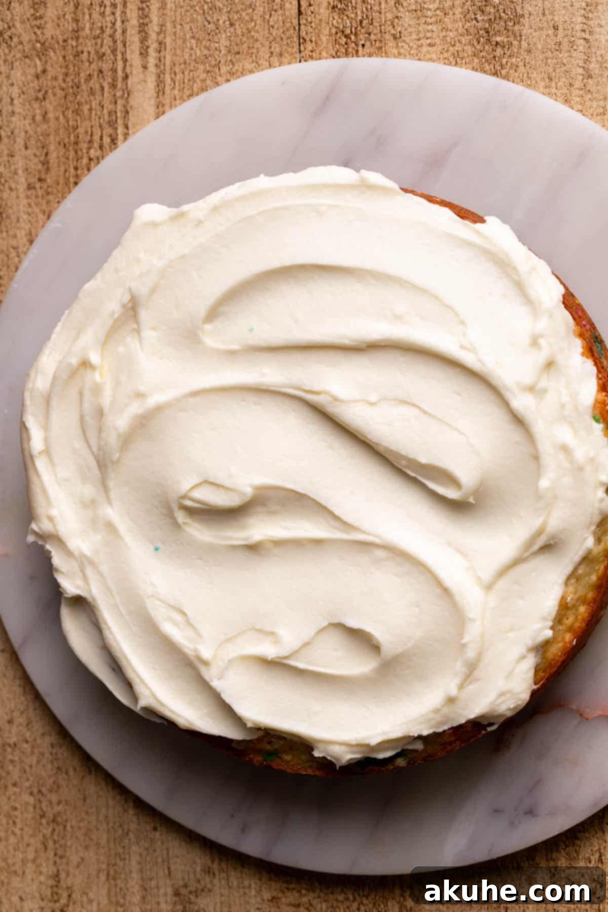 Festive Sprinkled Cake 8 Close-up of a cake layer with a thick, even layer of cream cheese frosting spread on top.