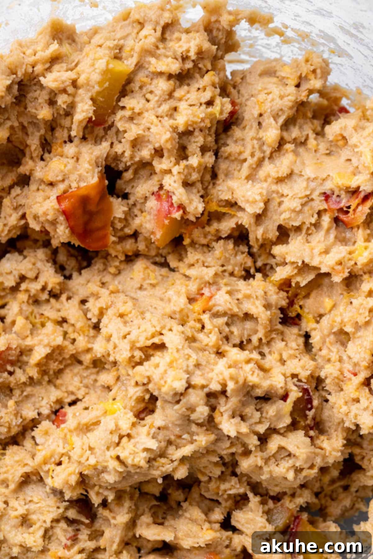 Sun-Kissed Peach Treats 7 Rich, peach-studded cookie dough resting in a clear glass bowl, showcasing its texture and ingredients.