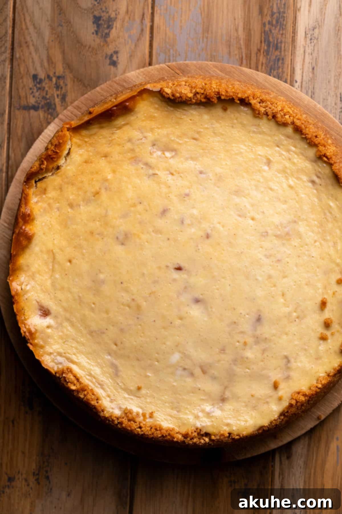 Luscious Peach Cheesecake 9 A golden-brown baked cheesecake resting on a wooden board, cooled and ready for chilling.