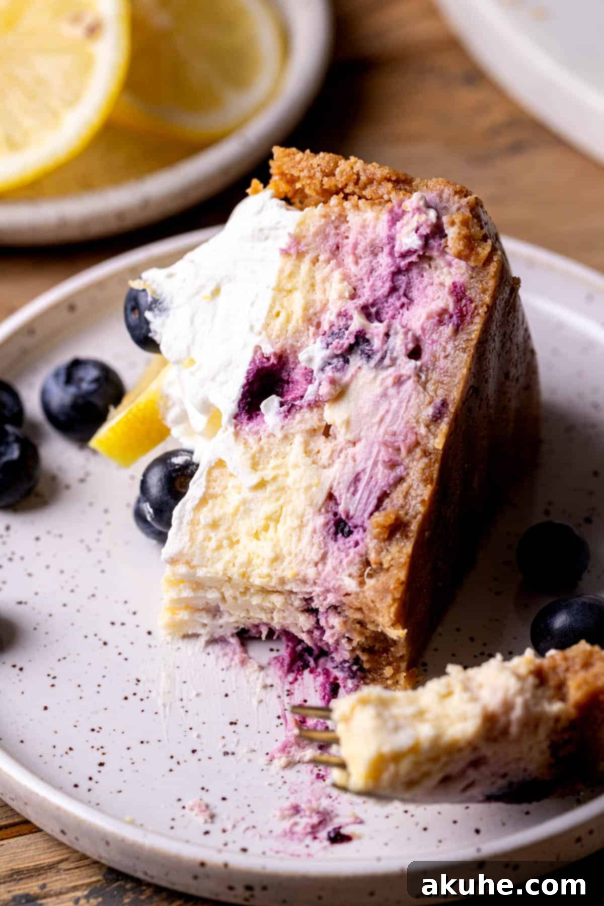 Zesty Lemon Blueberry Cheesecake 10 A slice of lemon blueberry cheesecake on a plate with a bite taken out, highlighting its deliciousness.