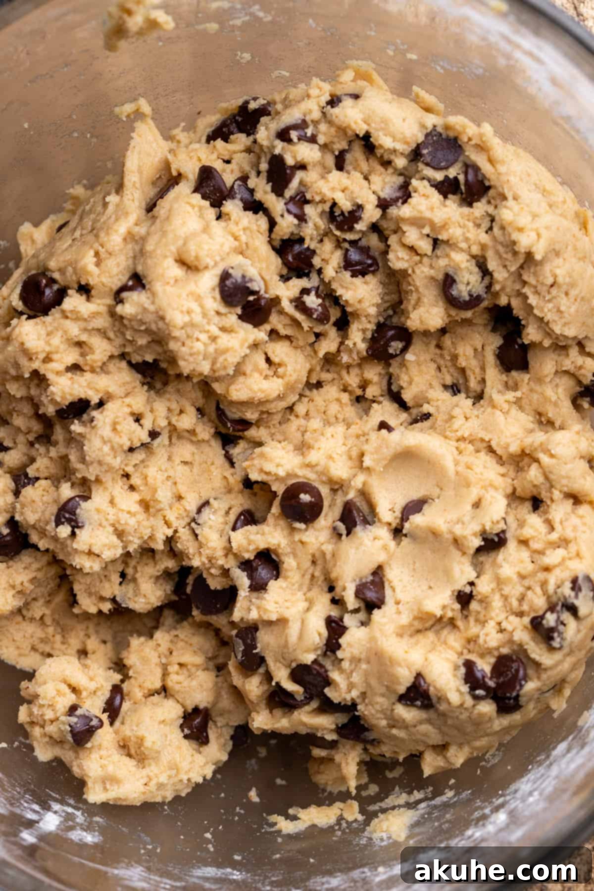 Freshly mixed cookie dough with chocolate chips in a clear glass bowl, showcasing its texture.