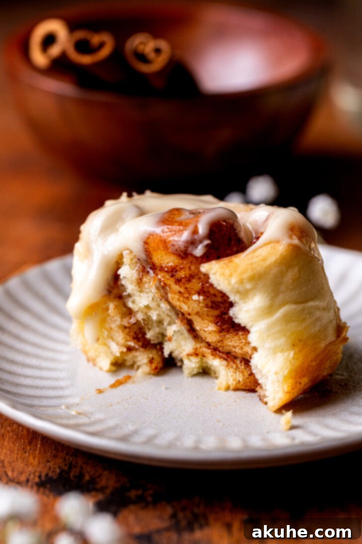 A mini cinnamon roll on a plate with a bite missing, showing the gooey interior.